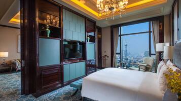 A spacious hotel room with a large bed, a television, a seating area with a view of the city, and a chandelier.