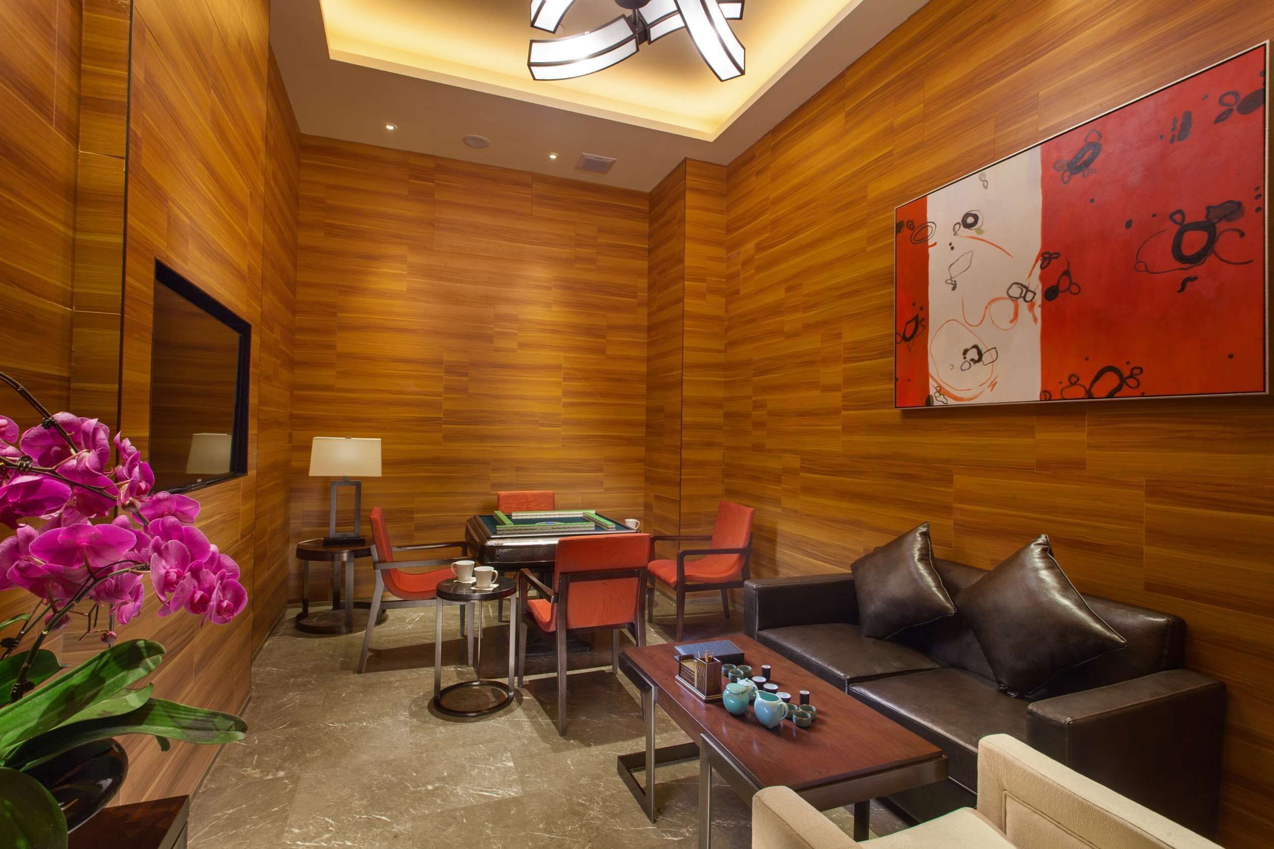 Un salón moderno con paneles de madera, mesa de billar, asientos cómodos y un cuadro abstracto grande.