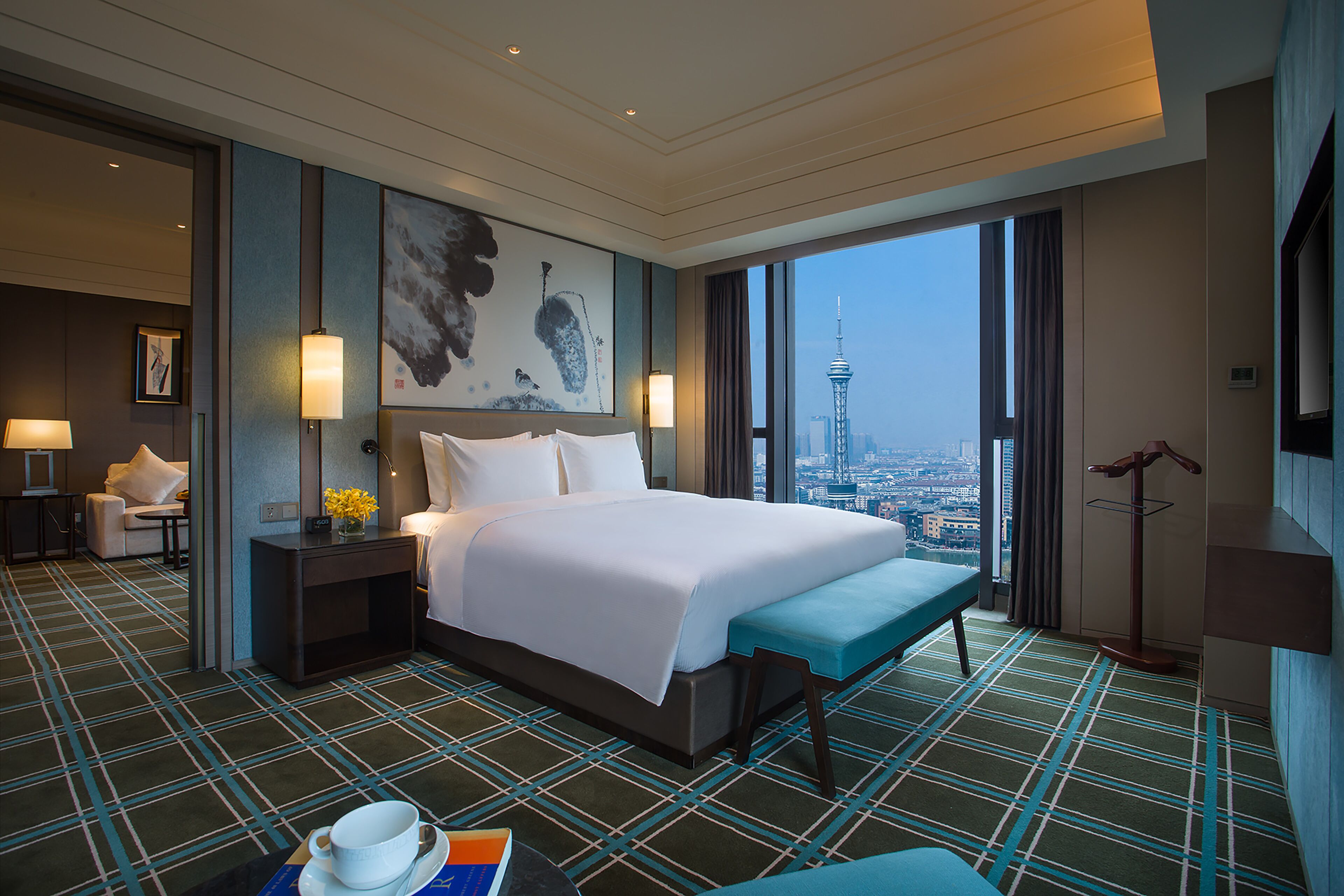 Hotelkamer met een groot bed, een bankje, een bureau en uitzicht op een stadsbeeld.