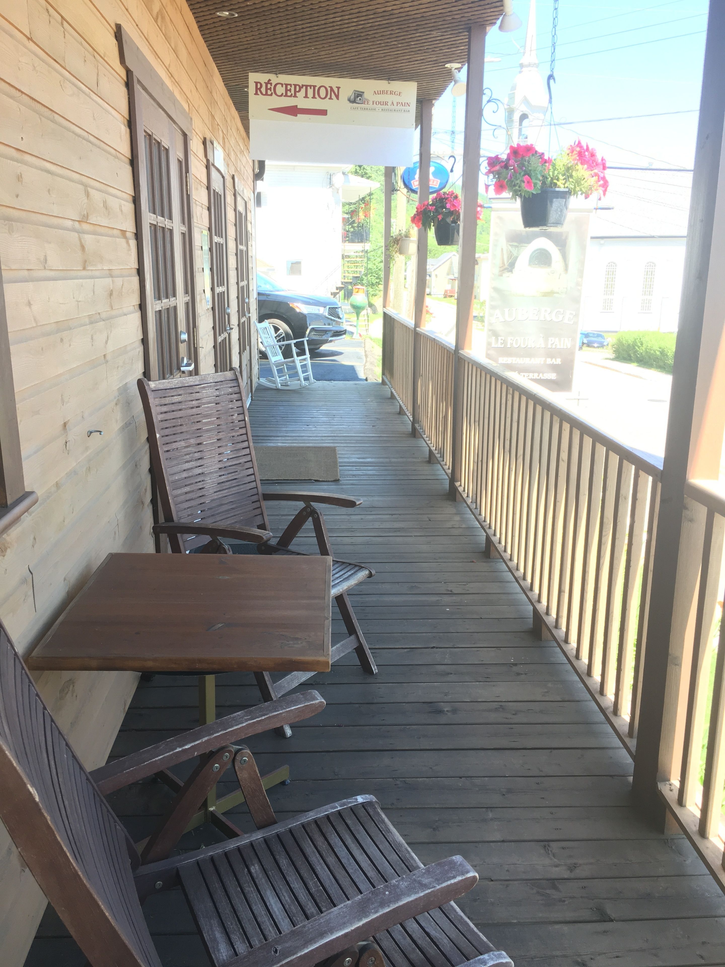 A wooden porch with a reception sign, outdoor seating, and a view of the street.