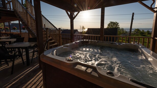 A hot tub on a wooden deck with a view of the sunset and a staircase leading to an upper level. - Auberge Le Four à Pain (Petite-Riviere-Saint-Francois)