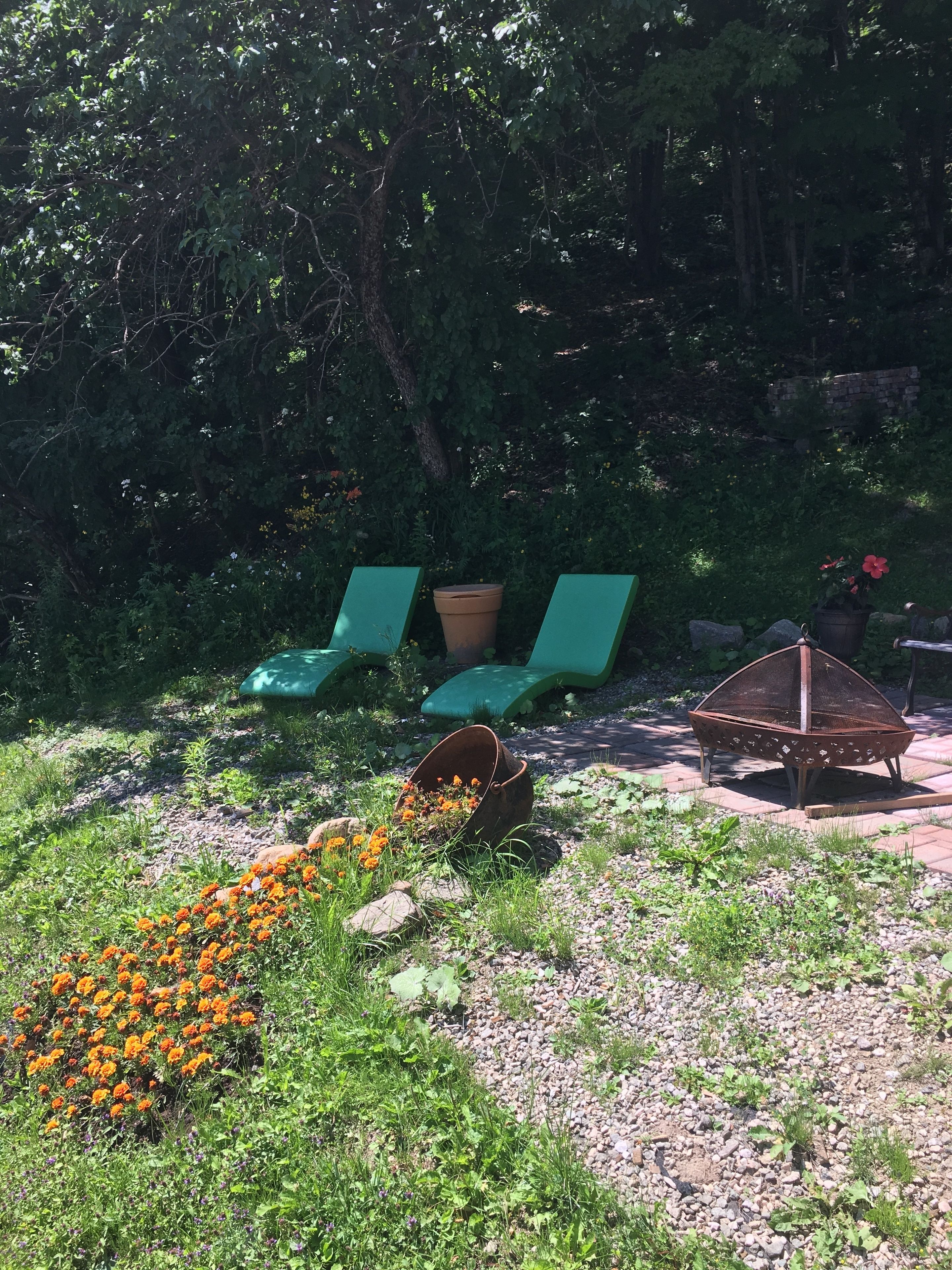 A garden area with green lounge chairs, a fire pit, and a flower bed with orange flowers.