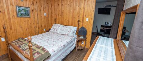 A wooden-paneled room with a bed, bedside table, and a mirror.