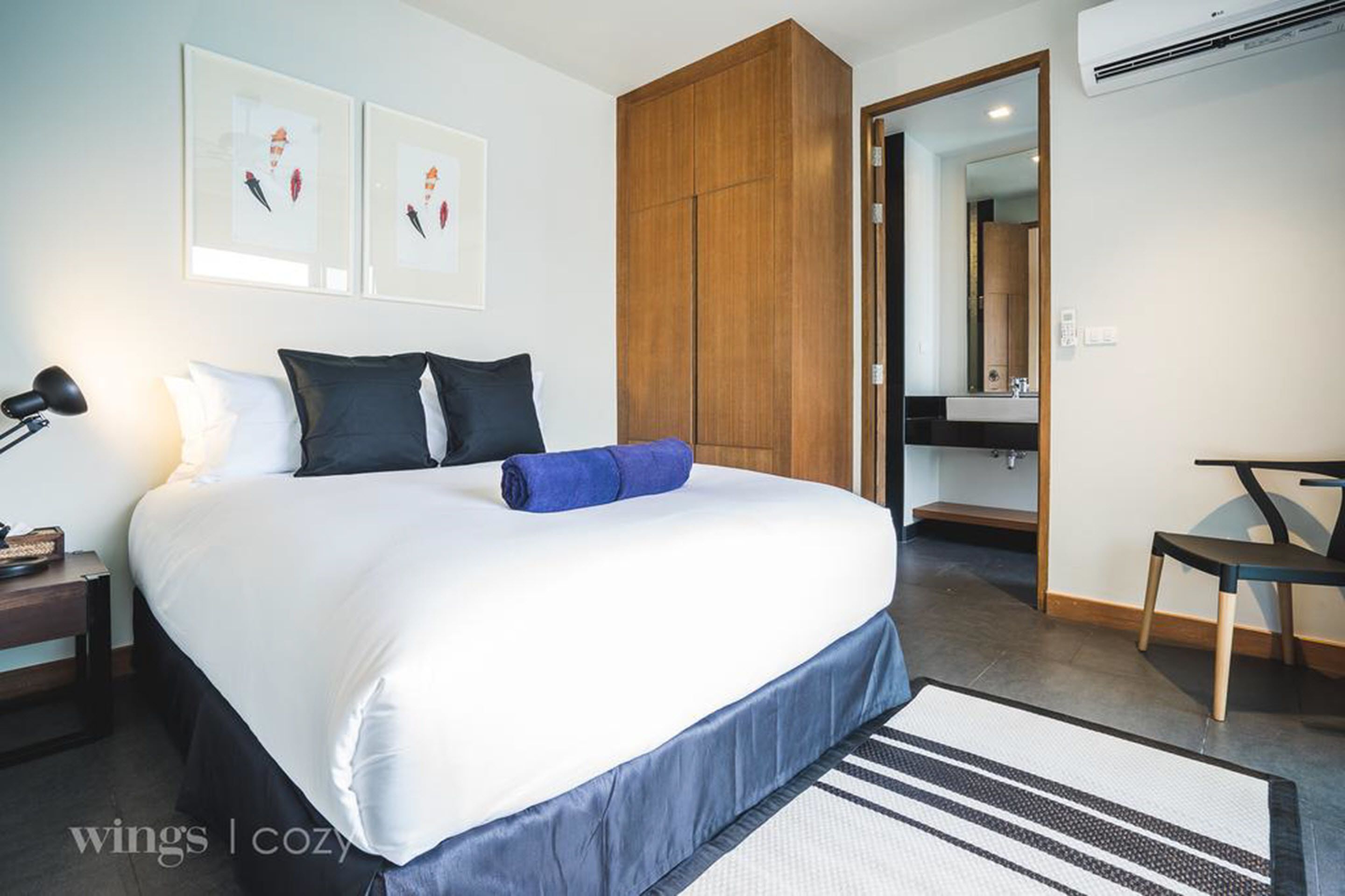 Ein Hotelzimmer mit einem großen Bett, einem Holzschrank, einem Schreibtisch mit Stuhl und einem durchgegangenen Türspalte sichtbar erkennbaren Badezimmer.