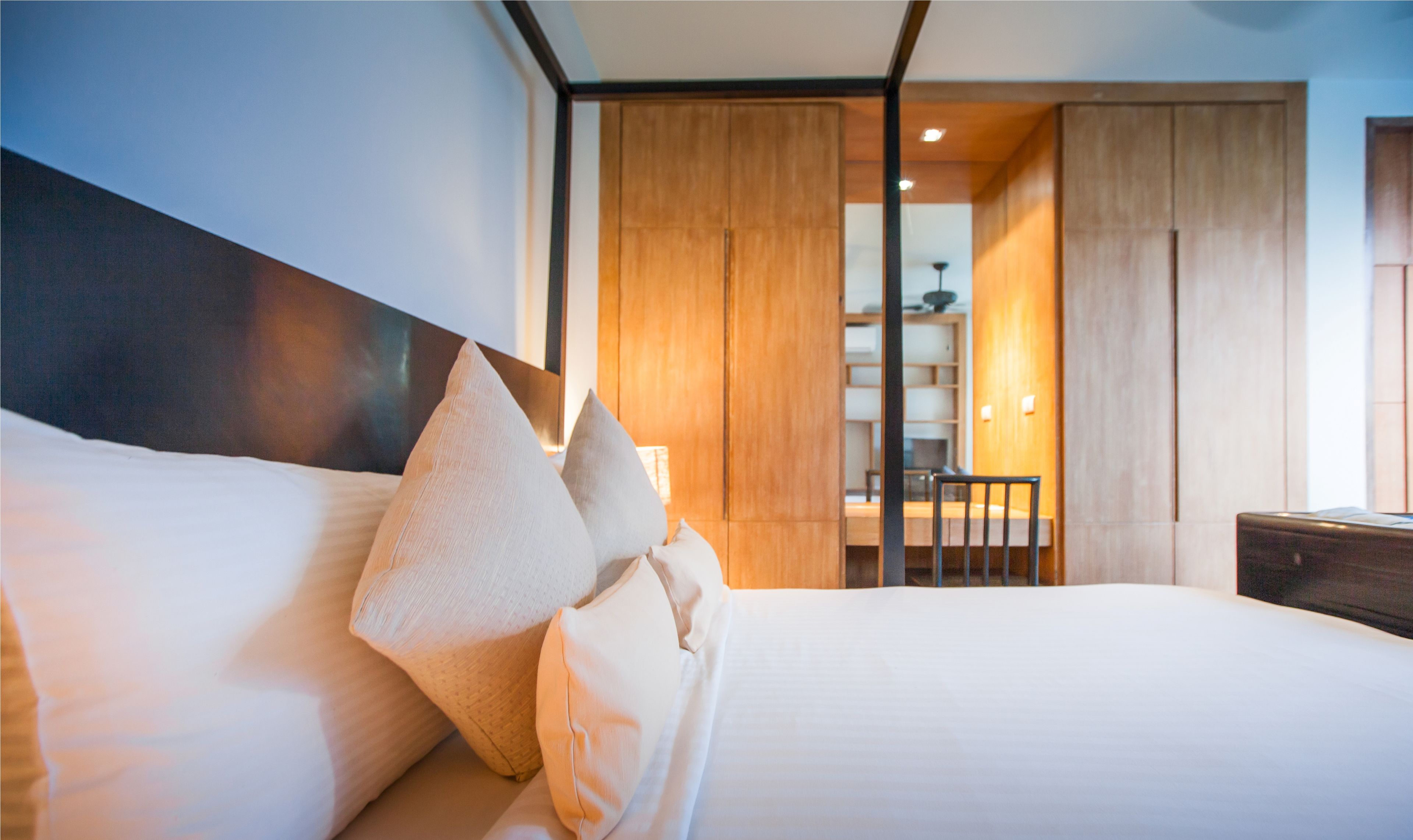 A modern hotel room with a neatly made bed, a wooden wardrobe, and a desk with a chair.