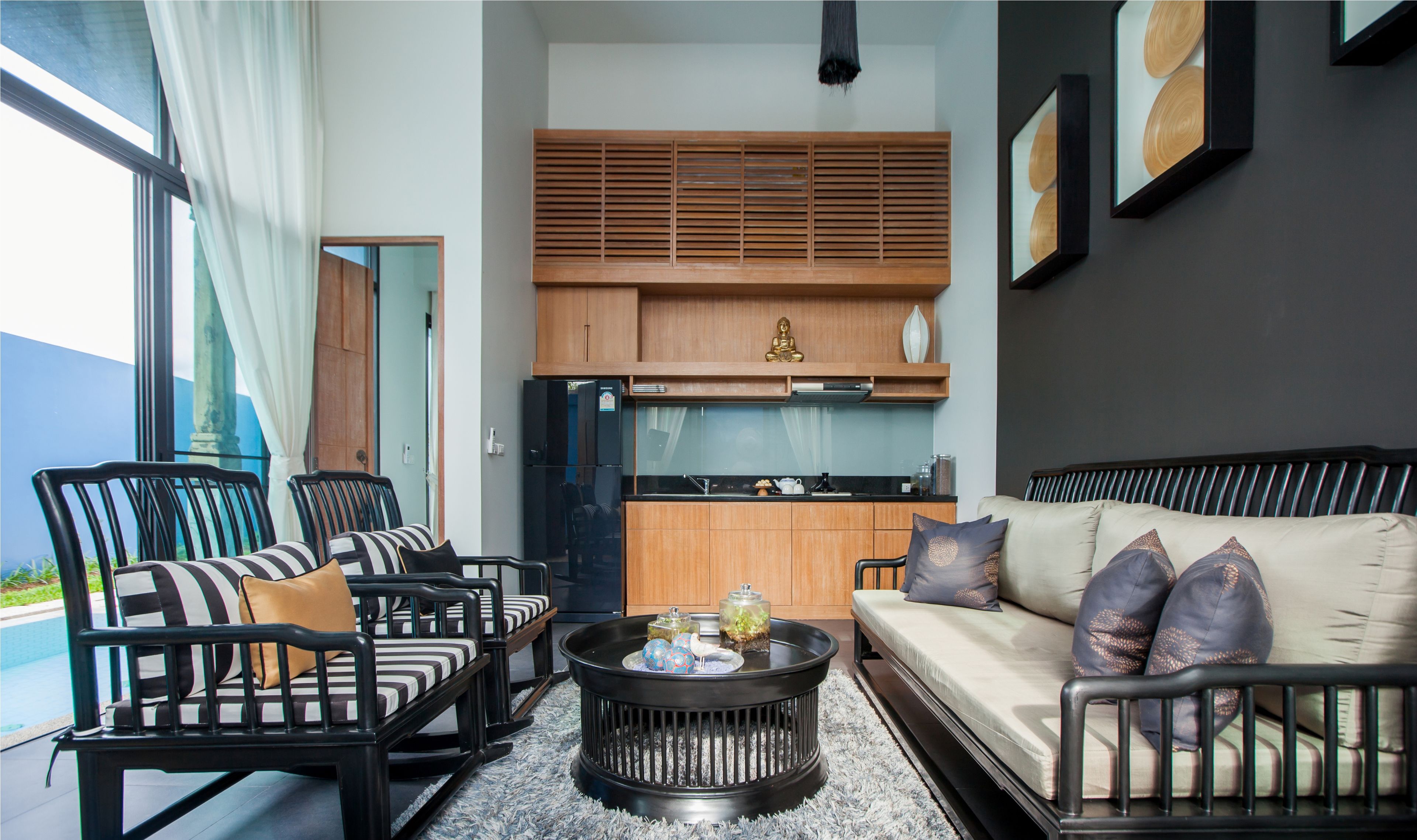 A modern living room with a sofa, chairs, a coffee table, and a kitchen area with wooden cabinets and a refrigerator.