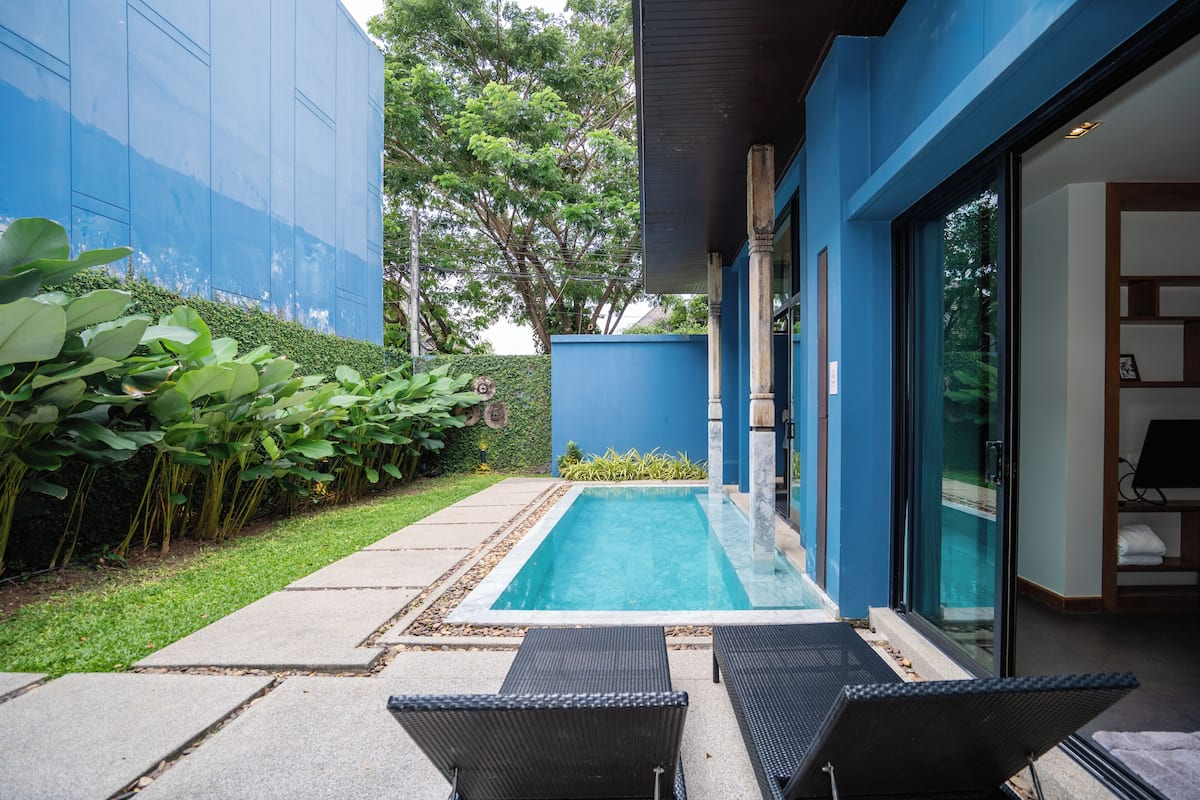 Un espace piscine extérieur moderne, doté d’une structure en verre, d’un mur bleu et d’un jardin bien entretenu.