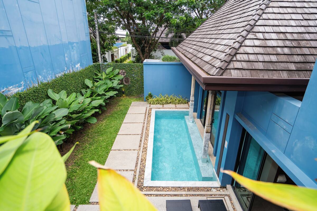 Une piscine rectangulaire dont les bords sont recouverts de carreaux, entourée d’une terrasse en béton et bordée d’une haie basse.