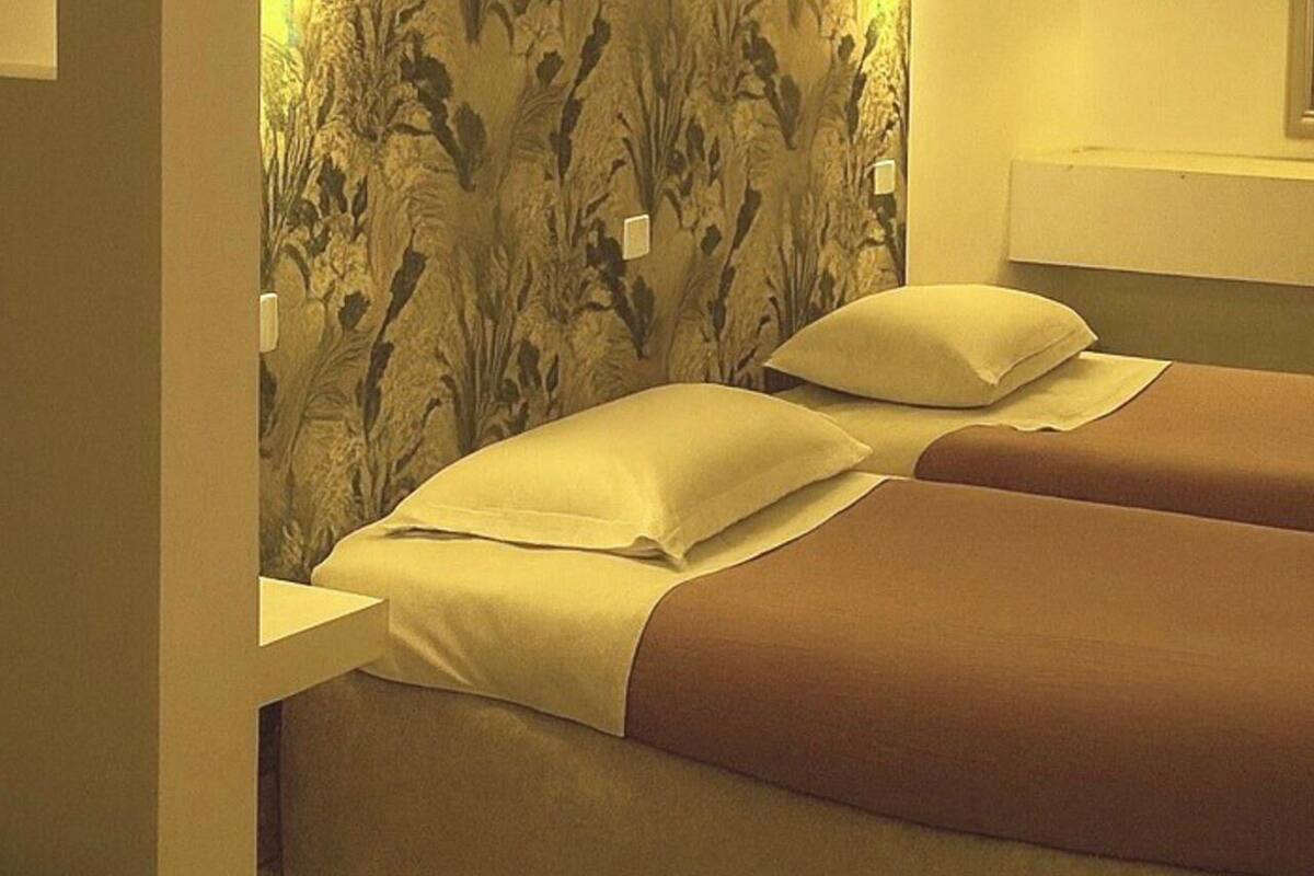 A room with two beds, each with a pillow and a blanket.