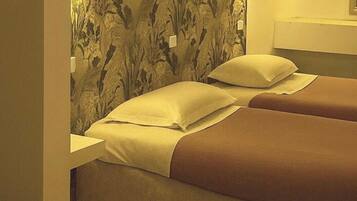 A room with two beds, each with a pillow and a blanket.