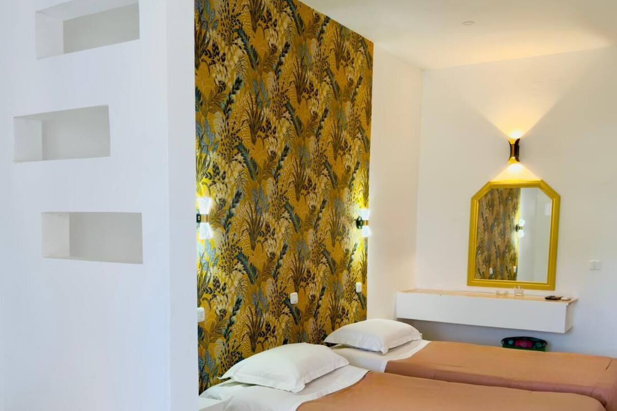 A bedroom with two beds, a large mirror, and a patterned wall.