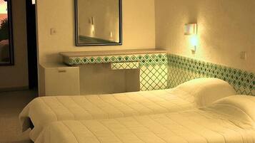A hotel room with a bed, a nightstand, a mirror, and a wall-mounted light fixture.
