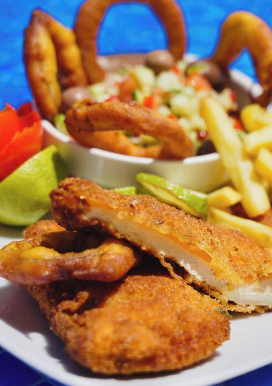 Un plato de filetes de pescado rebozados y fritos, acompañados de papas fritas y una ensalada pequeña.