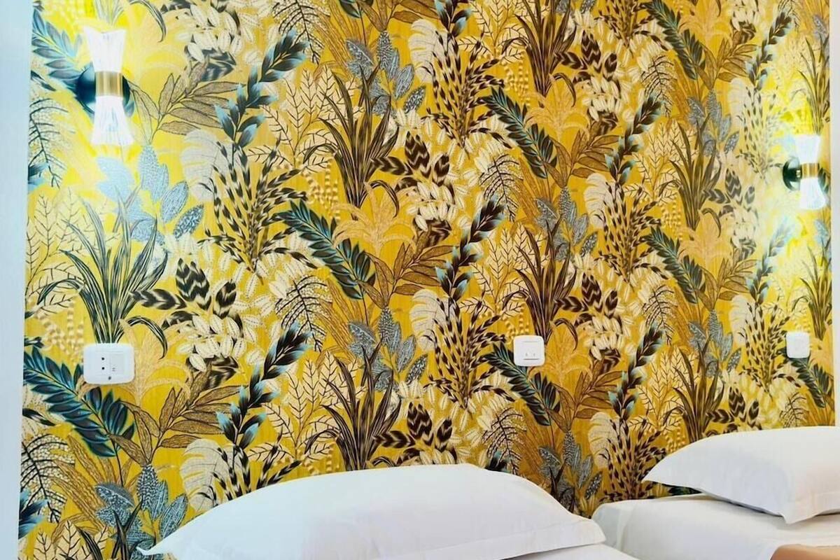 A hotel room with a floral wallpaper, two beds, and a nightstand with a lamp.