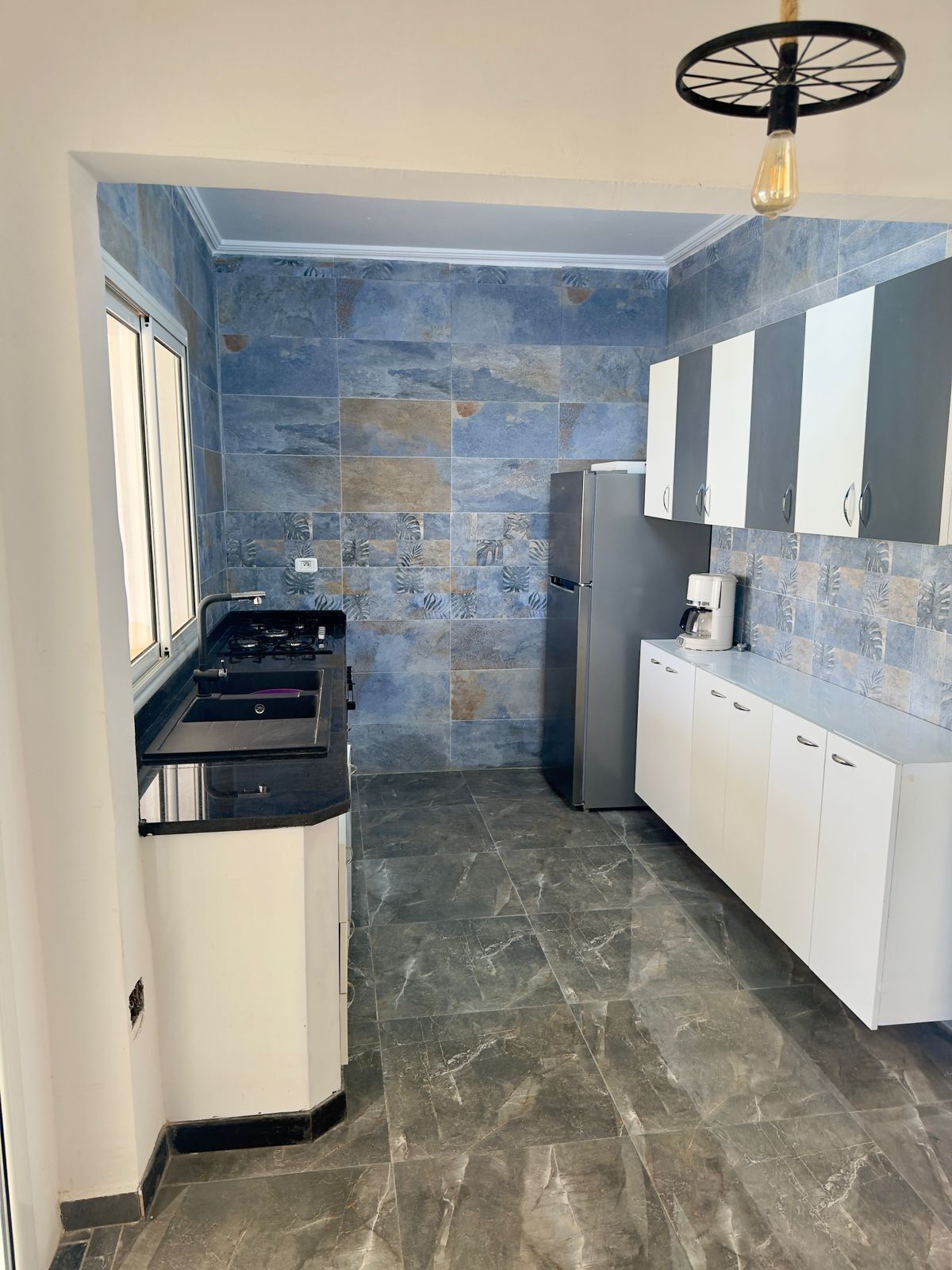 Una cocina compacta con estufa a gas, refrigerador y gabinetes blancos.