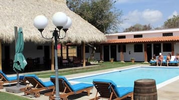 Un área de piscina con sillas de descanso y una estructura de techo de paja.