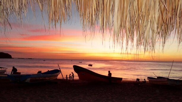 A beach with boats and people during sunset. - Machele' s Place Beachside Hotel & Pool (Tola)