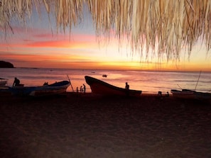 A beach with boats and people during sunset. - Machele' s Place Beachside Hotel & Pool (Tola)
