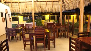 A restaurant with wooden tables and chairs, a thatched roof, and potted plants. - Machele' s Place Beachside Hotel & Pool (Tola)