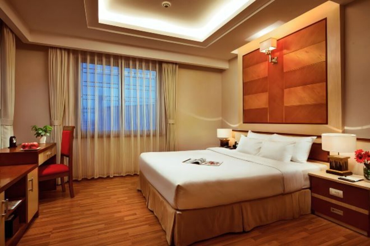 A hotel room with a bed, bedside tables, a desk, a chair, and a window with curtains.
