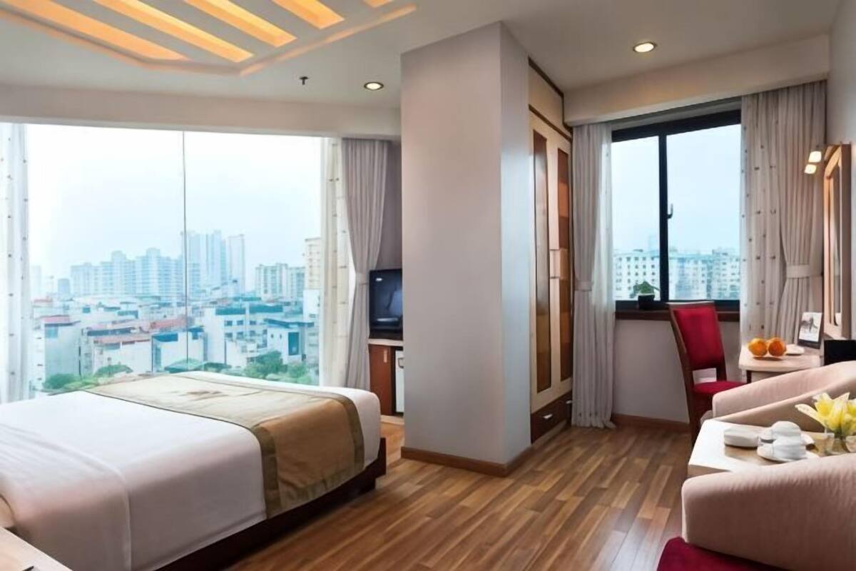 A hotel room with a large bed, a desk, a chair, and a view of the city.