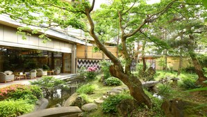 Un jardín japonés tradicional con un estanque de carpas koi, puentes de piedra y una zona de estar con sillas y mesas.