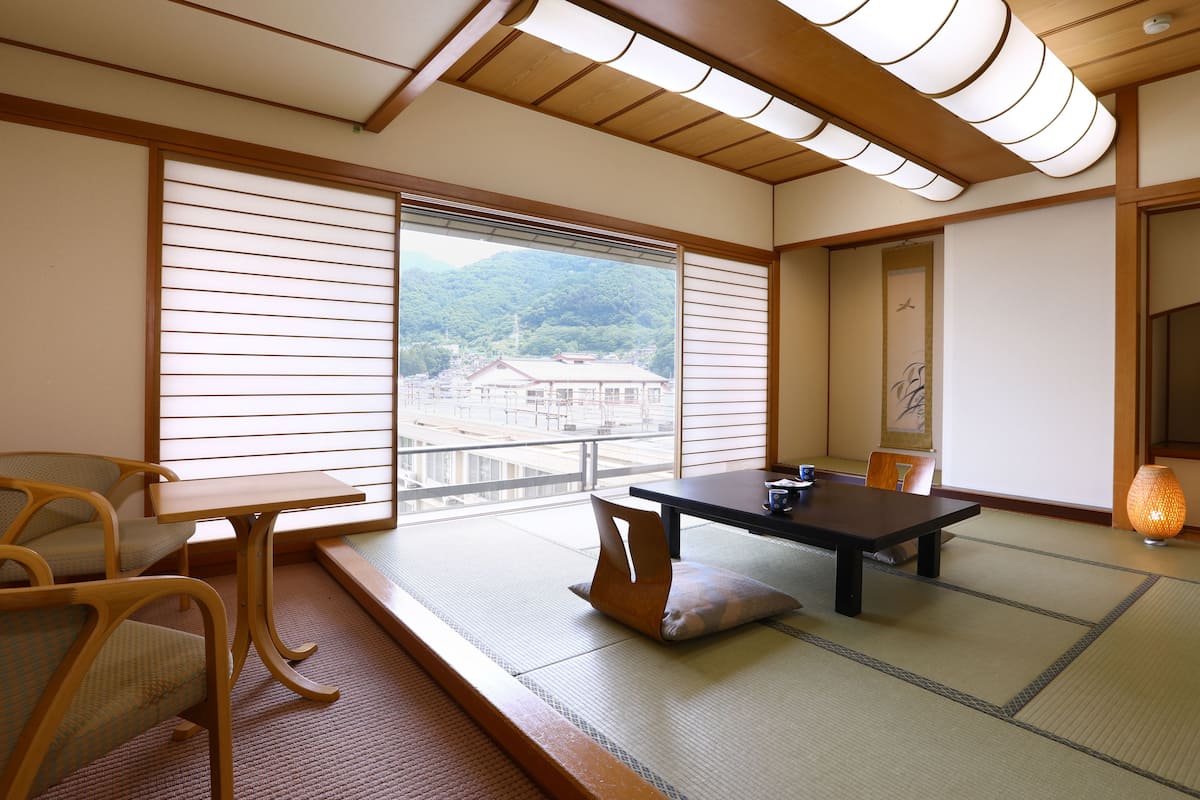 Una habitación tradicional japonesa con suelo de tatami, una mesa baja y vistas a un paisaje montañoso.