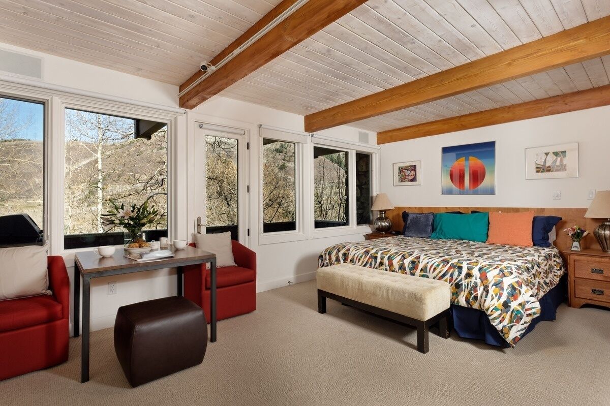 Een slaapkamer met een groot bed, een bureau, een stoel en een raam met uitzicht op bomen.