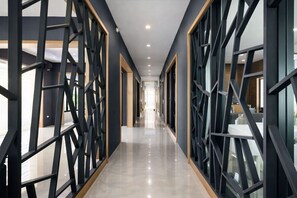 A modern hotel corridor with geometric black and gold decor, a polished floor, and large windows. - T.U.B. Mansion (Pak Kret)
