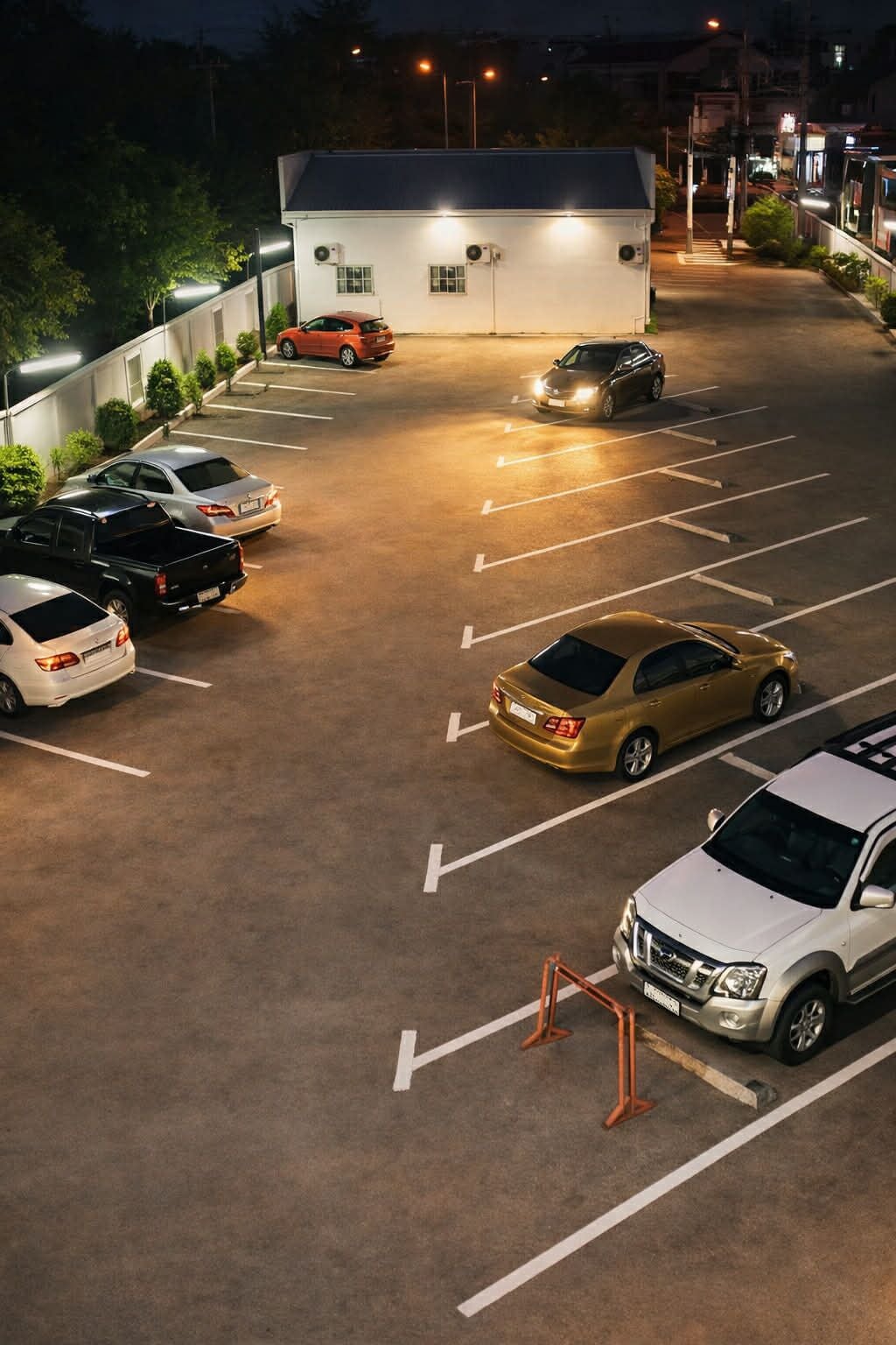 A parking lot with multiple cars, a building with a white facade, and a well-lit environment.