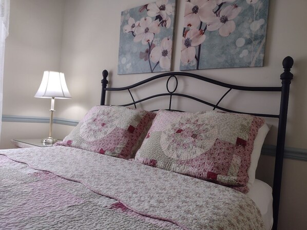 Una cama con cubrecolchón acolchado, una lámpara de noche y dos cuadros con motivos florales en la pared.