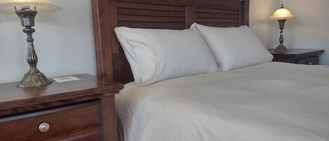 A neatly made bed with a wooden headboard, two bedside tables with lamps, and a wooden nightstand with drawers.