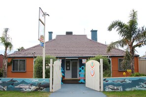 Una casa con techo de tejas, puerta principal y un portón con un mural de delfines.