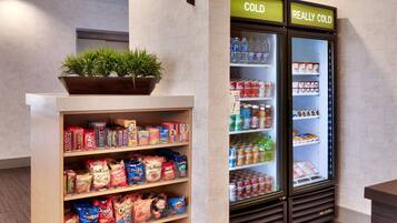 Zona de exhibición de snacks y bebidas con un letrero que dice “HOME 2 MKT” y dos refrigeradores etiquetados como “FRÍO” y “MUY FRÍO”.