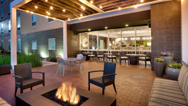An outdoor patio with a fire pit, seating, and a restaurant view. - Home2 Suites by Hilton Houston/Katy (Katy)