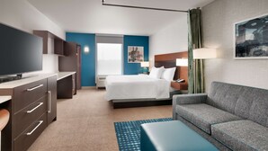A hotel room with a bed, a sofa, a TV, a desk, and a bathroom. - Home2 Suites by Hilton Houston/Katy (Katy)