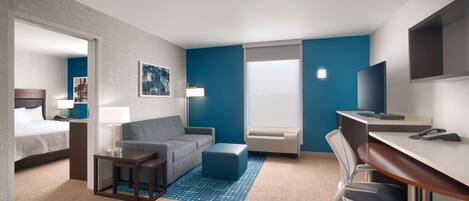 A hotel room with a bed, a sofa, a desk with a chair, a television, and a window with blinds.