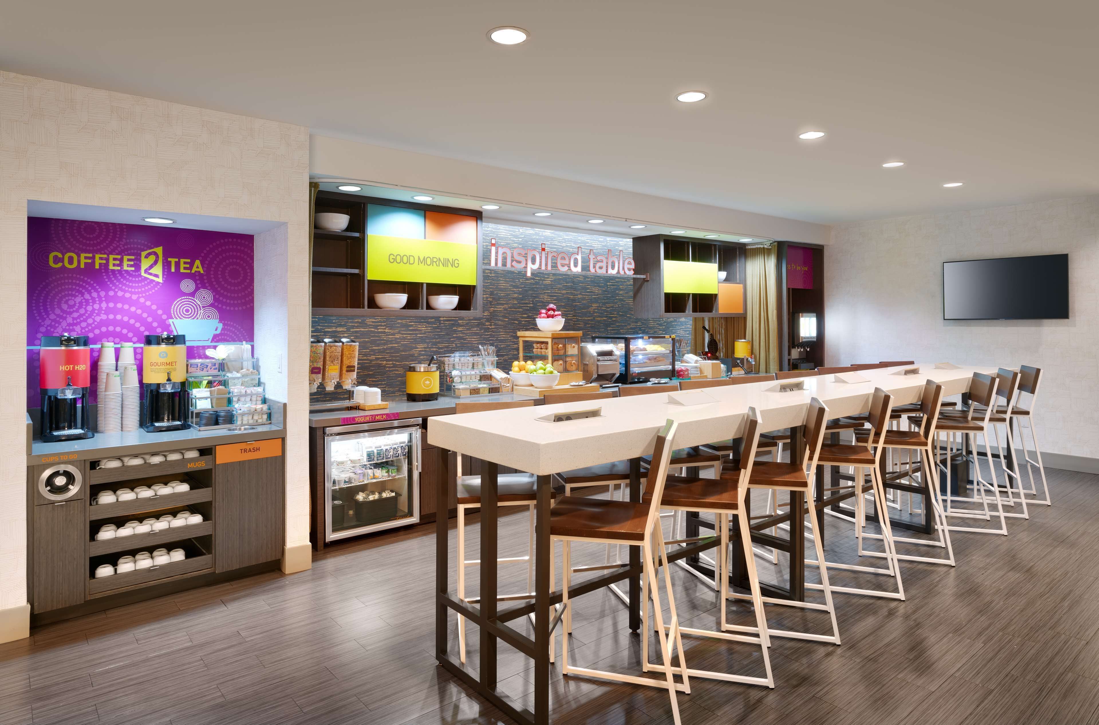 A modern coffee shop with a long counter, bar stools, and a variety of coffee and tea options.