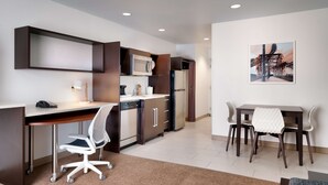 A modern kitchen with built-in appliances, a dining area with a table and chairs, and a painting on the wall. - Home2 Suites by Hilton Houston/Katy (Katy)
