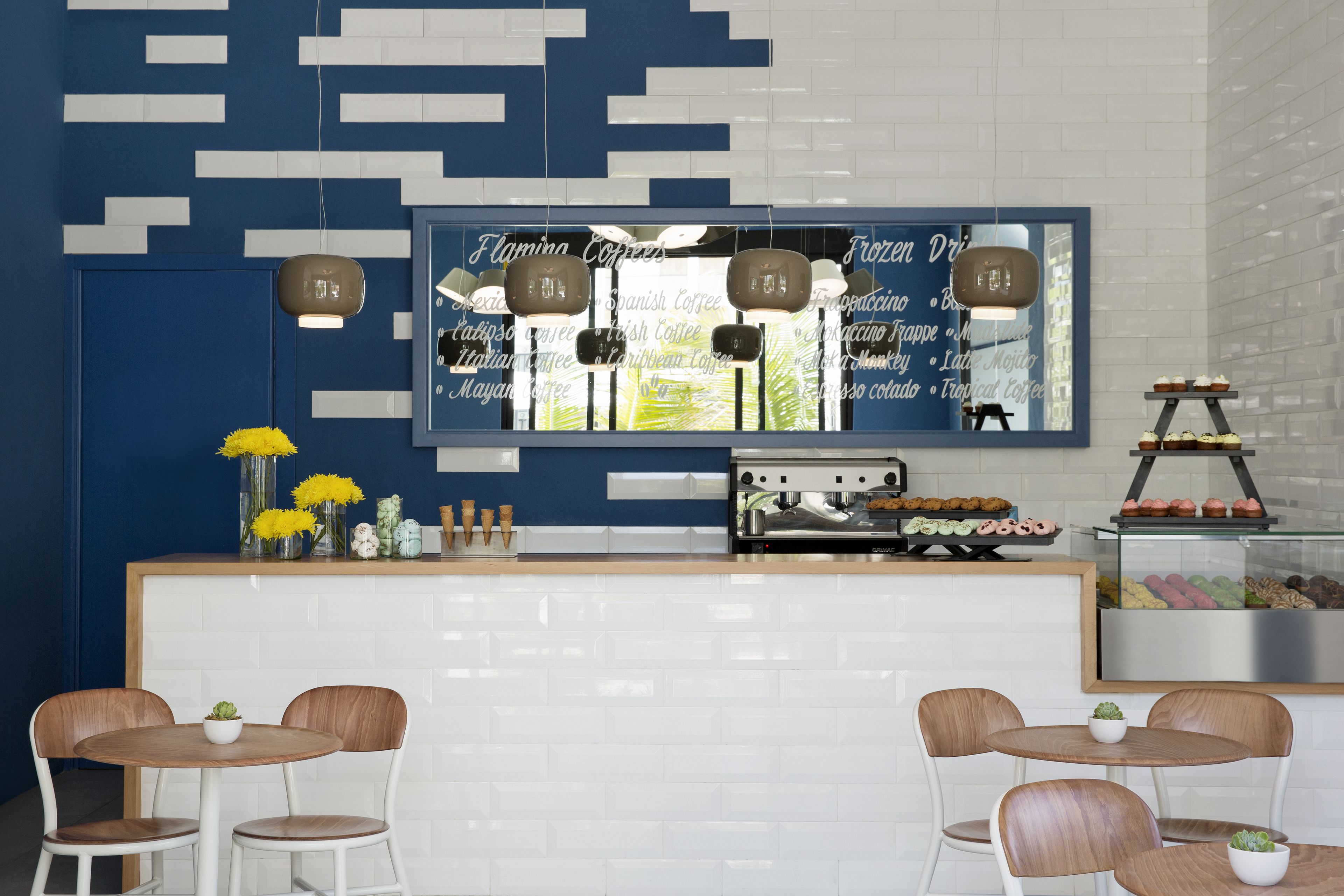 Una cafetería moderna con una decoración azul y blanca, que presenta un menú grande, una máquina de café y una vitrina con pasteles.