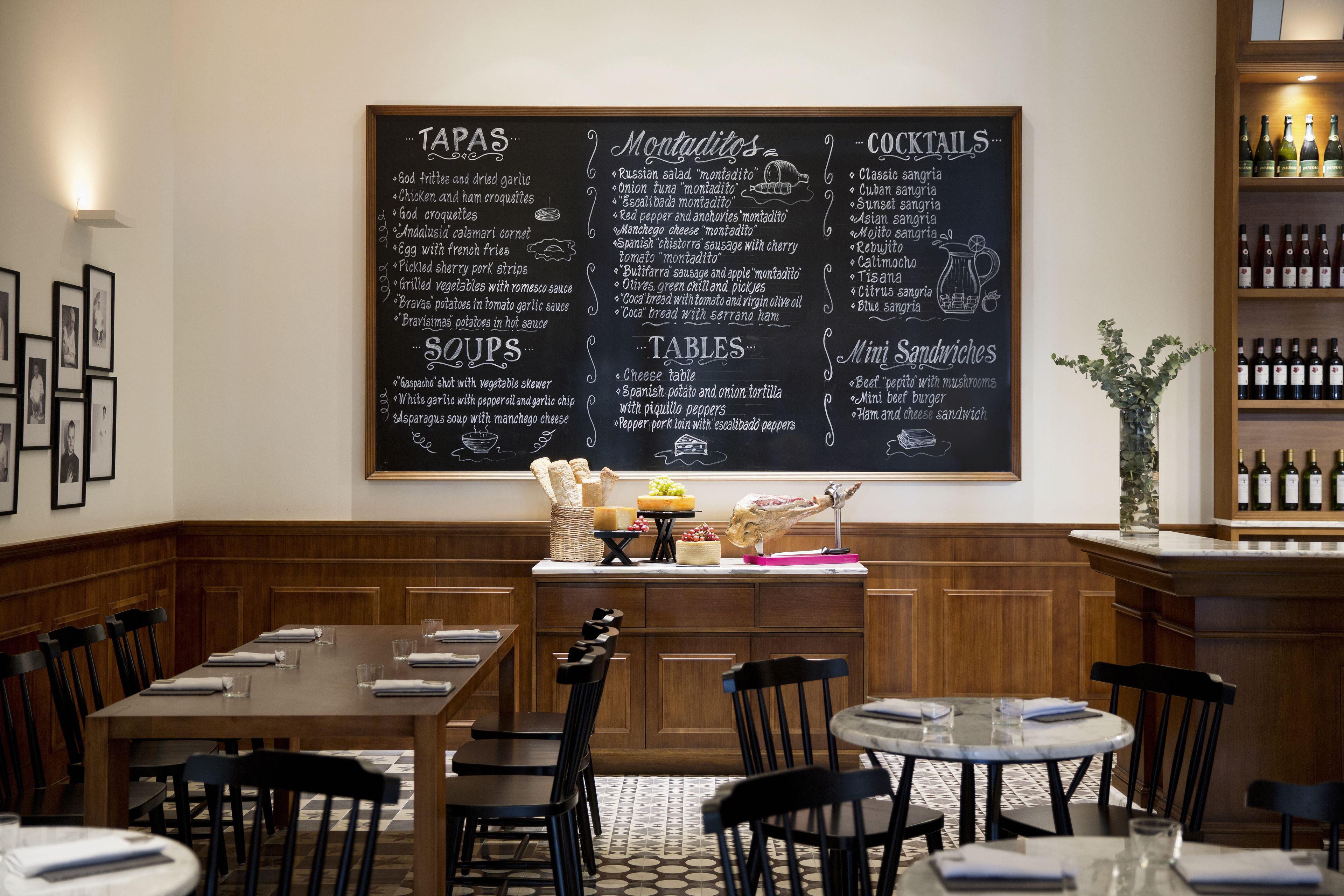 A restaurant with a chalkboard menu listing tapas, montaditos, cocktails, soups, and tables.