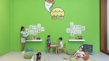 Una habitación luminosa y colorida con paredes verdes, una pizarra con dibujos infantiles y sillones de peluche.