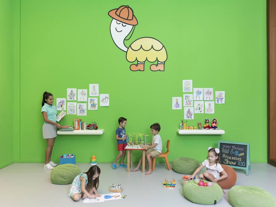 Una habitación luminosa y colorida con paredes verdes, una pizarra con dibujos infantiles y sillones de peluche.