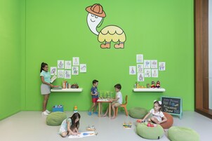 Una stanza dai colori vivaci, con pareti verdi, una lavagna con disegni di bambini e sacchi di fagioli.