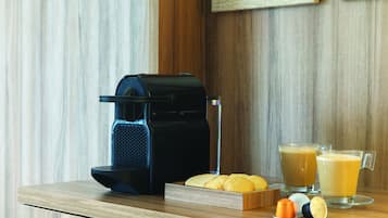 Une machine à café, deux verres de café, une assiette de biscuits et une dosette de café sur une table en bois.