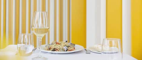 A dining table with a plate of pasta, two glasses of white wine, and a fork.