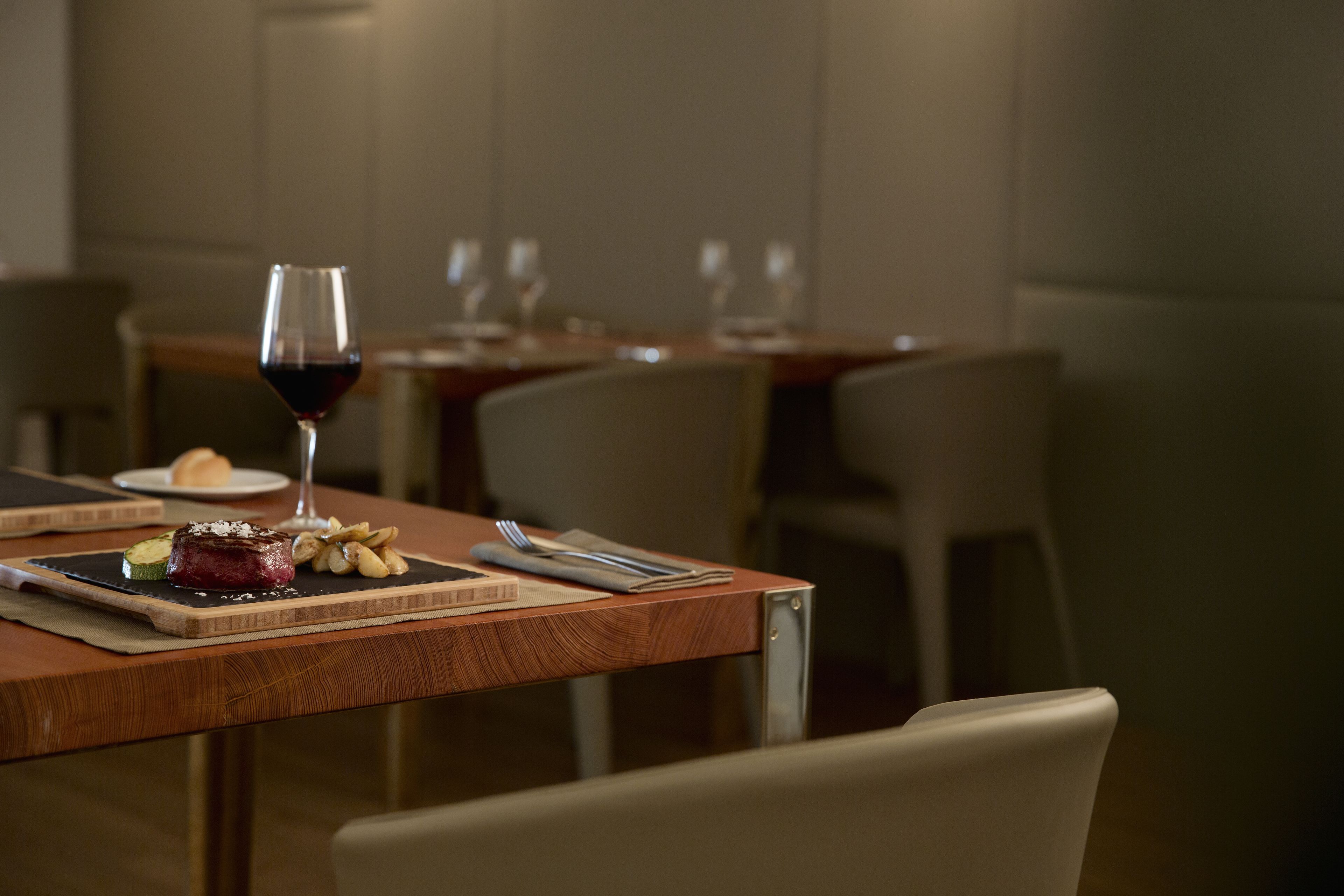 Una mesa de comedor con un bistec, verduras y una copa de vino tinto.