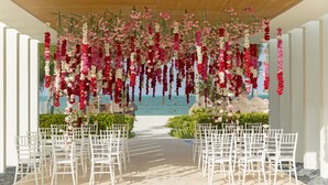 An outdoor wedding venue with white chairs arranged in rows, a floral arch, and a view of the beach. - Finest Playa Mujeres by The Excellence Collection - All Inclusive (Punta Sam)