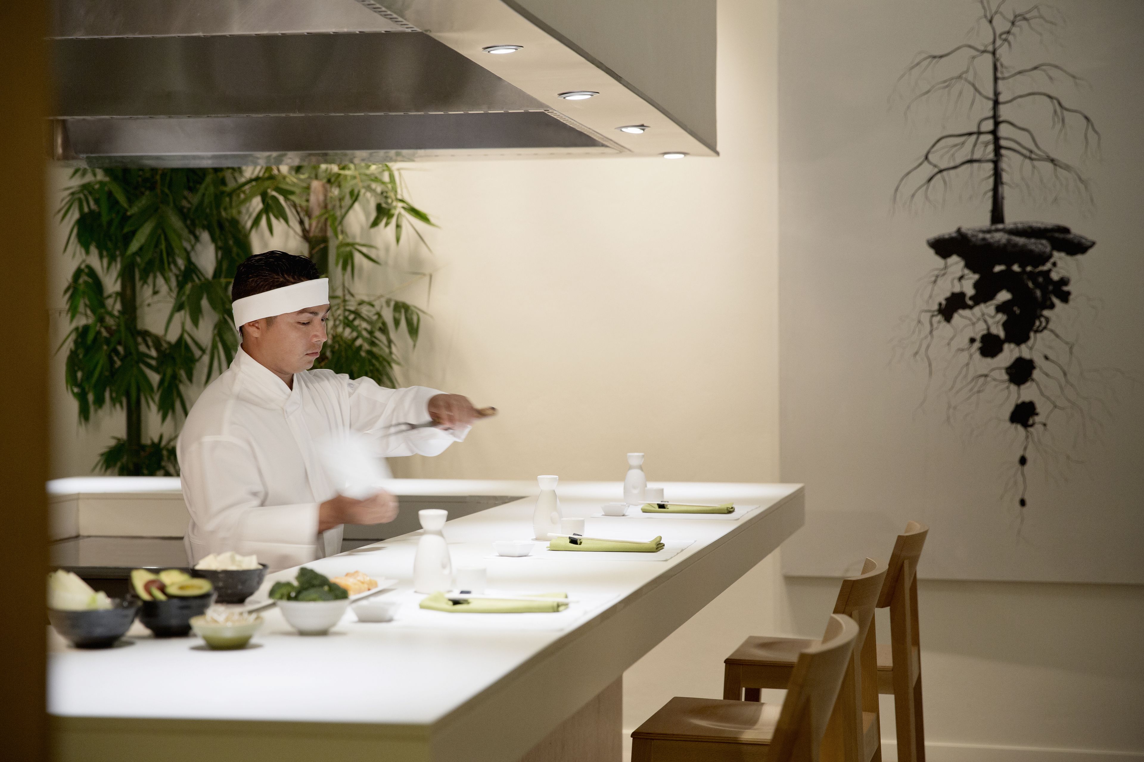 A chef in a white uniform preparing food at a long, white counter with various bowls and utensils.