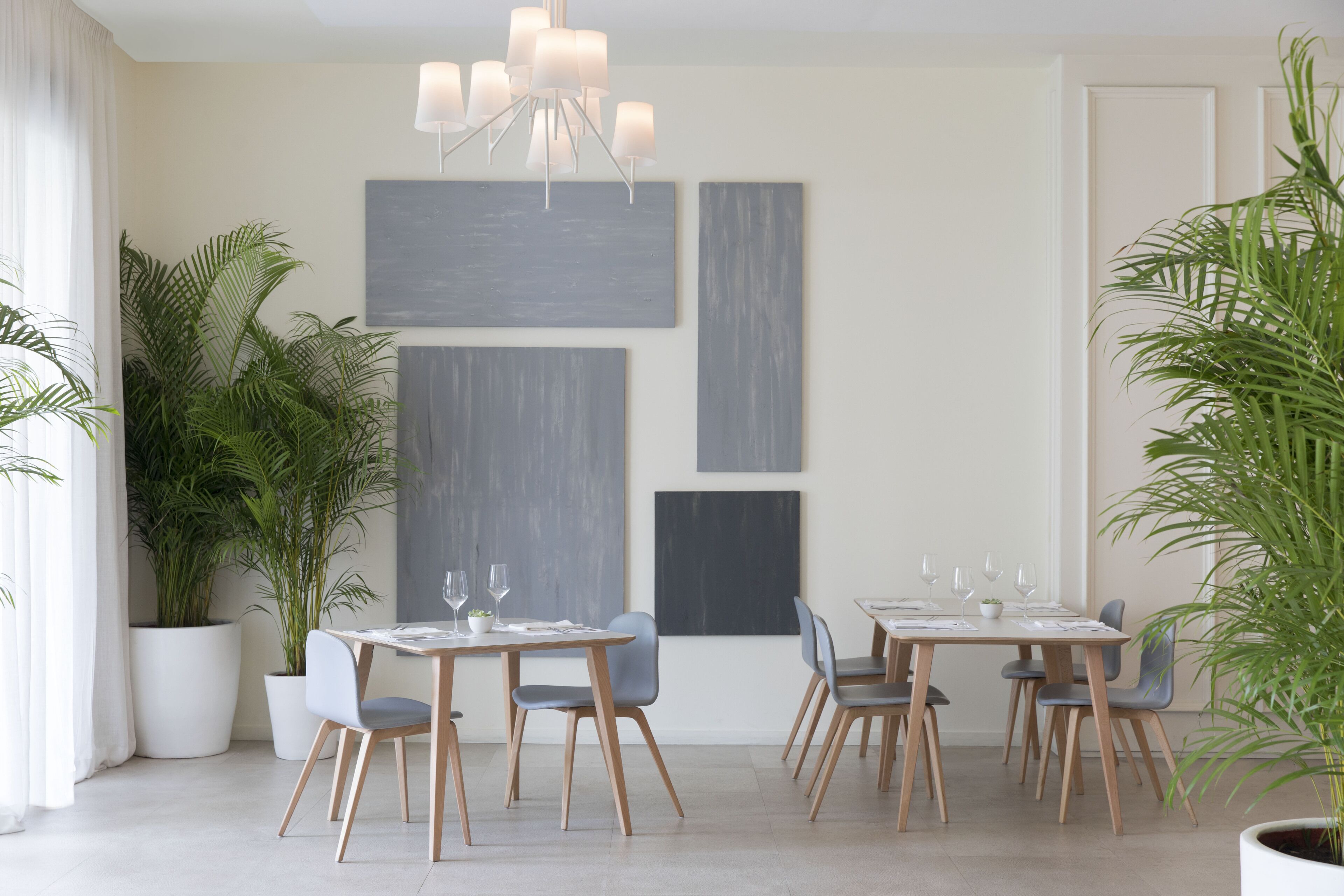 A modern dining area with two tables, chairs, and potted plants.